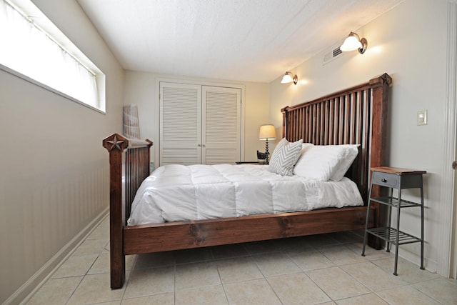 bedroom with tile patterned floors, visible vents, a textured ceiling, a closet, and baseboards