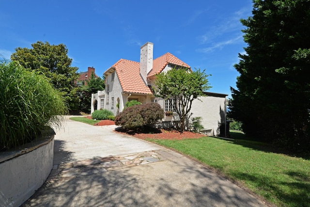 view of side of property featuring a chimney, stucco siding, a tiled roof, and a lawn