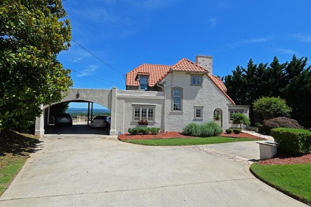 view of front of property featuring a detached carport, driveway, stucco siding, a chimney, and a tile roof