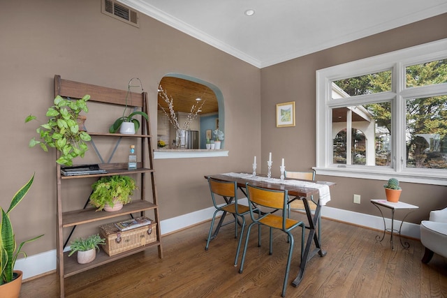 dining room with visible vents, wood finished floors, arched walkways, crown molding, and baseboards