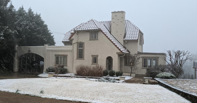 view of front of house featuring stucco siding, a chimney, and a tiled roof