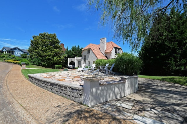 exterior space with stucco siding, a patio, a chimney, and a tiled roof