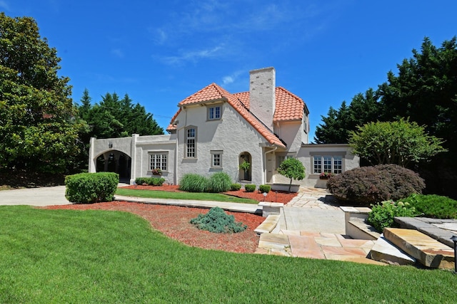 back of house featuring a chimney, stucco siding, a tile roof, and a yard