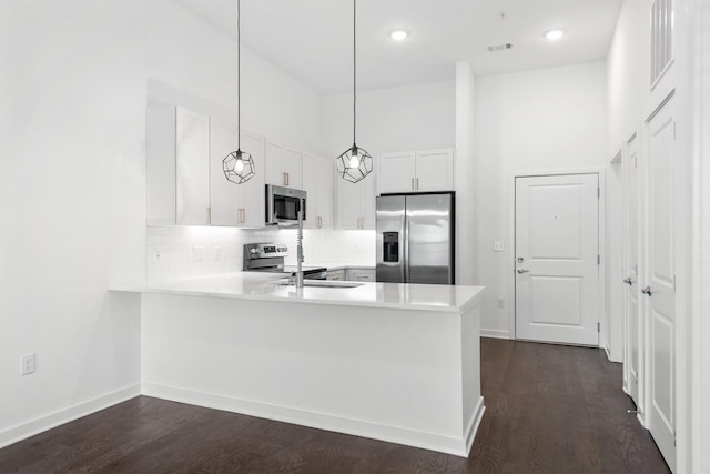 kitchen featuring a peninsula, stainless steel appliances, decorative backsplash, dark wood-type flooring, and light countertops