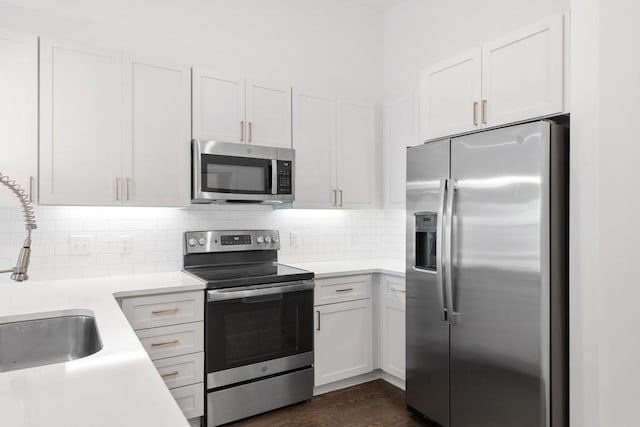 kitchen with dark wood finished floors, a sink, light countertops, appliances with stainless steel finishes, and backsplash