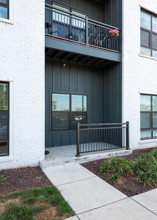 entrance to property featuring brick siding, covered porch, board and batten siding, and a balcony