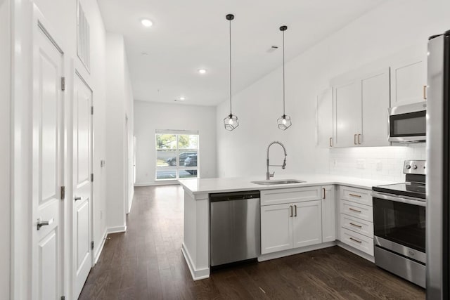 kitchen with decorative backsplash, appliances with stainless steel finishes, a peninsula, dark wood-style floors, and a sink