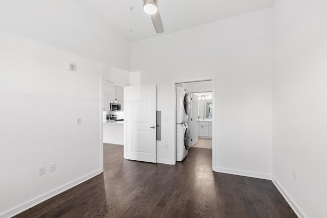 empty room with dark wood-type flooring, baseboards, stacked washer and clothes dryer, and ceiling fan