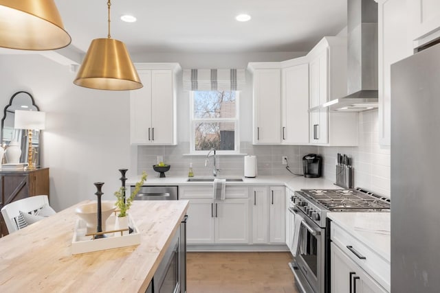 kitchen featuring tasteful backsplash, wall chimney range hood, appliances with stainless steel finishes, white cabinetry, and a sink