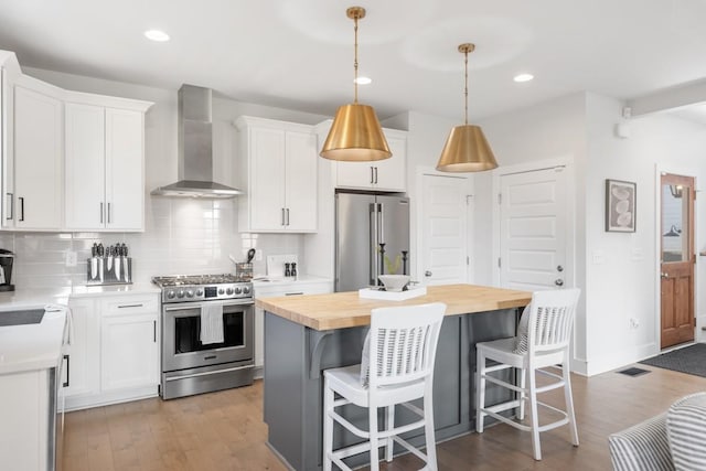 kitchen with tasteful backsplash, a center island, wall chimney range hood, appliances with stainless steel finishes, and wood counters