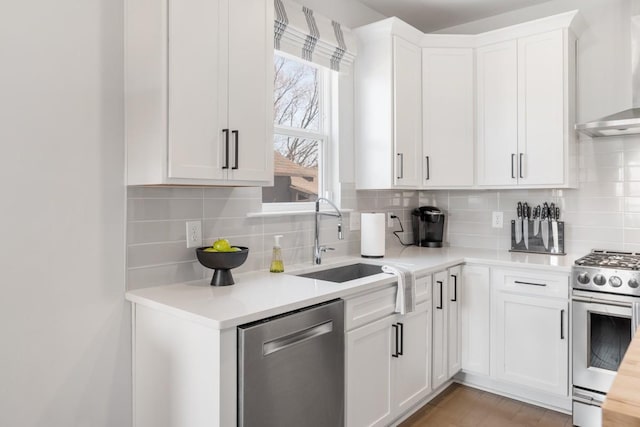 kitchen with a sink, wall chimney range hood, stainless steel appliances, white cabinets, and light countertops