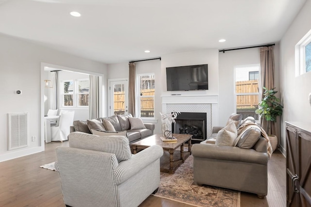 living area with a tiled fireplace, recessed lighting, wood finished floors, and visible vents