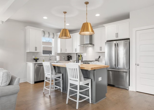 kitchen featuring butcher block counters, decorative backsplash, appliances with stainless steel finishes, wall chimney exhaust hood, and a center island