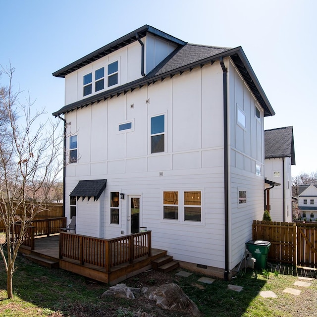 back of property with board and batten siding, a shingled roof, fence, a deck, and crawl space