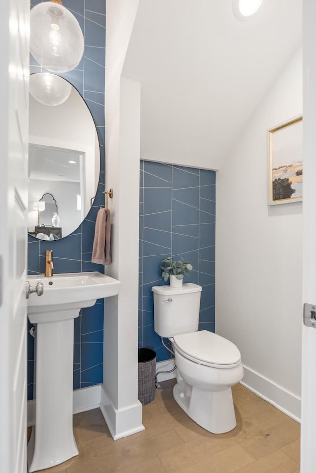 half bath featuring tile walls, toilet, wood finished floors, and vaulted ceiling