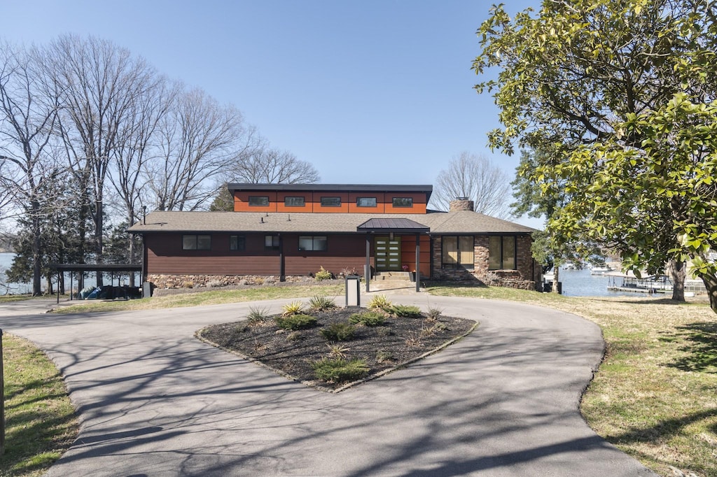 view of front of home featuring stone siding, curved driveway, and a chimney