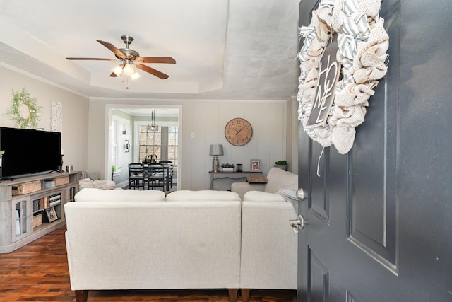 living room with a raised ceiling, dark wood-style flooring, and ceiling fan