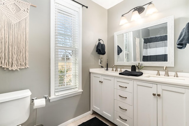 bathroom with a sink, baseboards, toilet, and double vanity