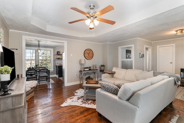 living area featuring a tray ceiling, dark wood-type flooring, ceiling fan, and ornamental molding