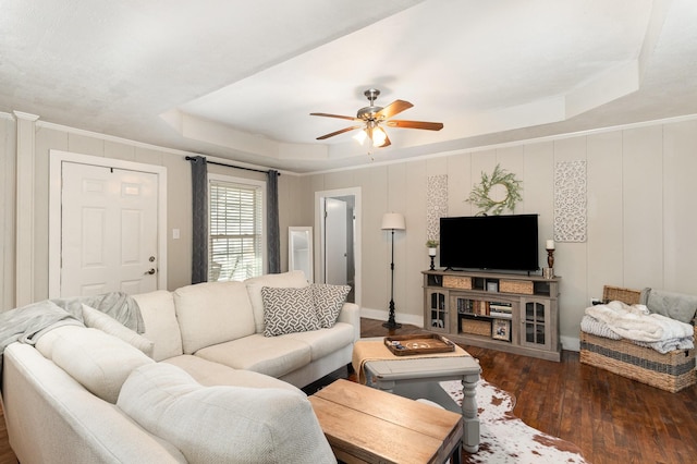 living area featuring a raised ceiling, hardwood / wood-style flooring, a decorative wall, and ceiling fan