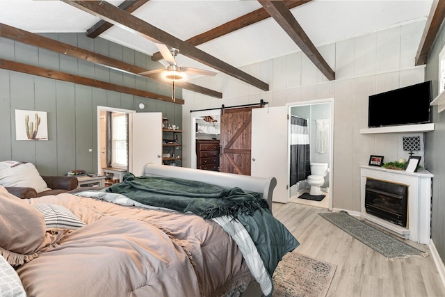 bedroom featuring a barn door, vaulted ceiling with beams, wood finished floors, and connected bathroom