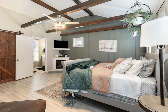 bedroom featuring multiple windows, lofted ceiling with beams, a barn door, and wood finished floors