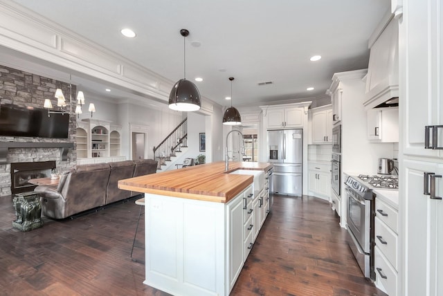 kitchen with butcher block counters, a kitchen bar, appliances with stainless steel finishes, white cabinets, and a sink