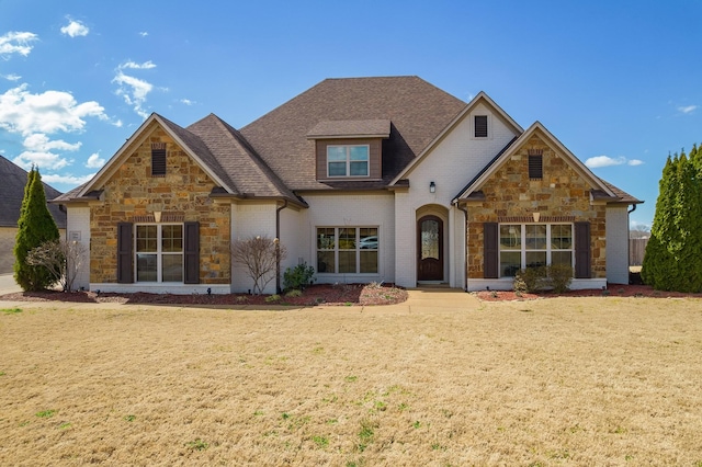 view of front of home featuring a front yard, brick siding, stone siding, and a shingled roof