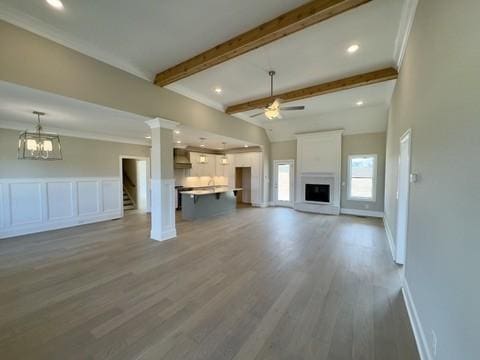 unfurnished living room featuring wood finished floors, a ceiling fan, beam ceiling, ornamental molding, and a decorative wall