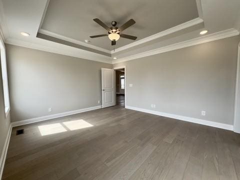 unfurnished room featuring a tray ceiling, dark wood-type flooring, ceiling fan, and crown molding