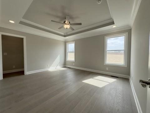 empty room with a ceiling fan, a raised ceiling, wood finished floors, and crown molding