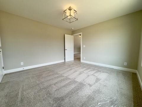 unfurnished room featuring an inviting chandelier, baseboards, and carpet floors