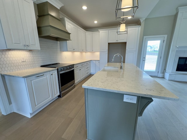 kitchen with stainless steel electric range, a sink, custom range hood, white cabinets, and tasteful backsplash