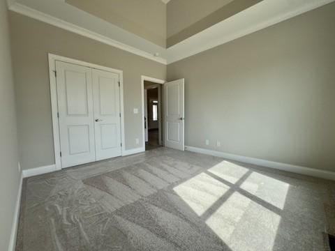 unfurnished bedroom featuring carpet, baseboards, a high ceiling, ornamental molding, and a closet