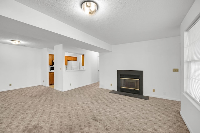 unfurnished living room featuring a textured ceiling, a fireplace with flush hearth, baseboards, and light carpet