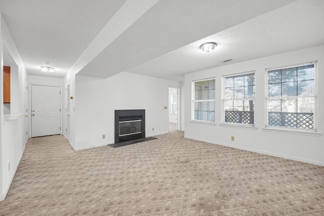 unfurnished living room featuring baseboards, visible vents, a fireplace with flush hearth, a textured ceiling, and carpet flooring