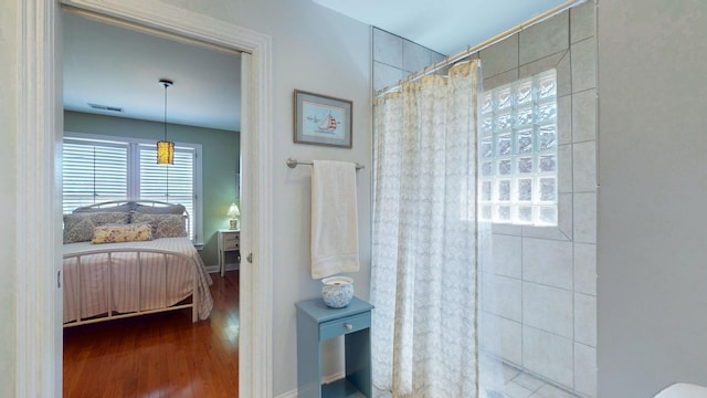 ensuite bathroom featuring visible vents, connected bathroom, tiled shower, and wood finished floors