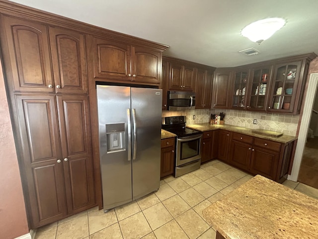 kitchen with tasteful backsplash, visible vents, glass insert cabinets, light tile patterned flooring, and stainless steel appliances