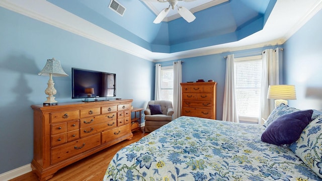 bedroom with a ceiling fan, a tray ceiling, wood finished floors, and visible vents