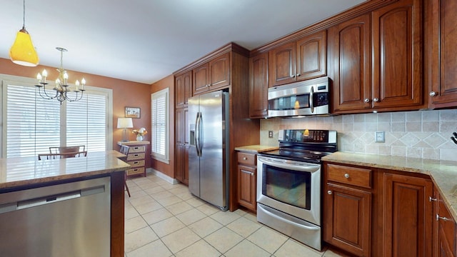 kitchen with light stone counters, stainless steel appliances, an inviting chandelier, and decorative backsplash