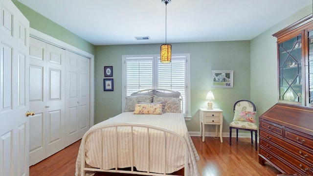 bedroom featuring a closet, visible vents, baseboards, and wood finished floors