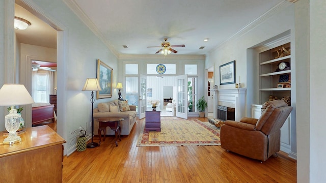 living room featuring built in shelves, light wood-style floors, a ceiling fan, and crown molding