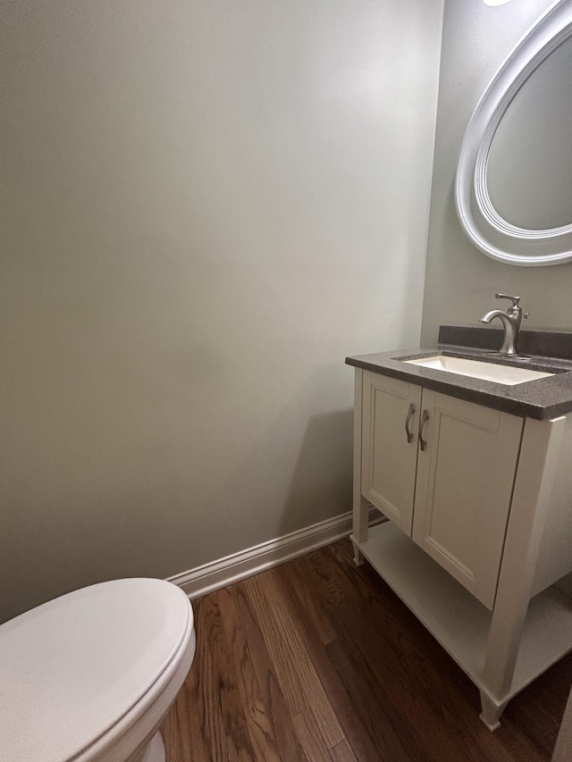 half bath featuring toilet, vanity, baseboards, and wood finished floors