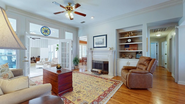 living area featuring light wood-style flooring, built in shelves, crown molding, and a ceiling fan