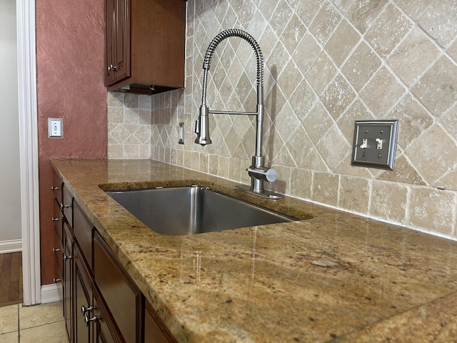 kitchen featuring a sink, stone countertops, backsplash, light tile patterned floors, and baseboards