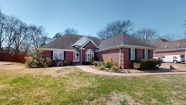 view of front of property with a front lawn, fence, brick siding, and roof with shingles