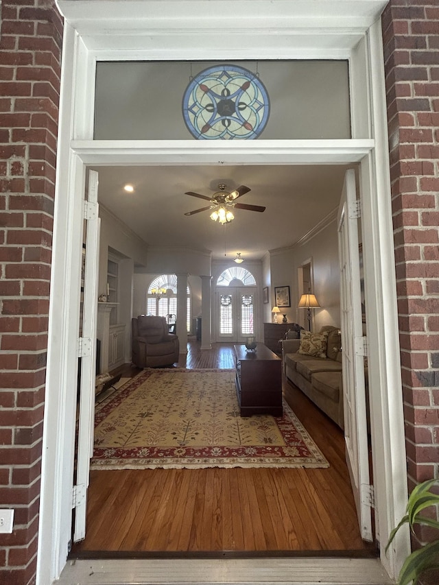 foyer with brick wall, ceiling fan, ornamental molding, french doors, and wood-type flooring