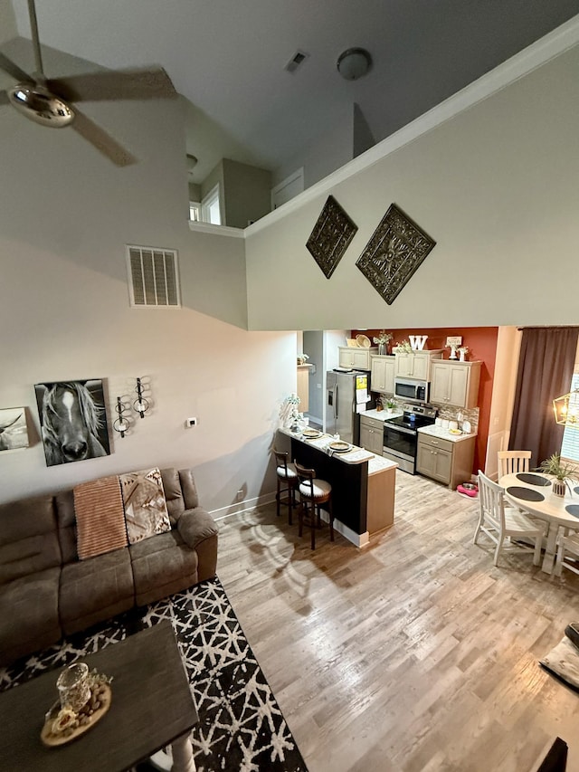 living room featuring visible vents, a high ceiling, a ceiling fan, and light wood finished floors