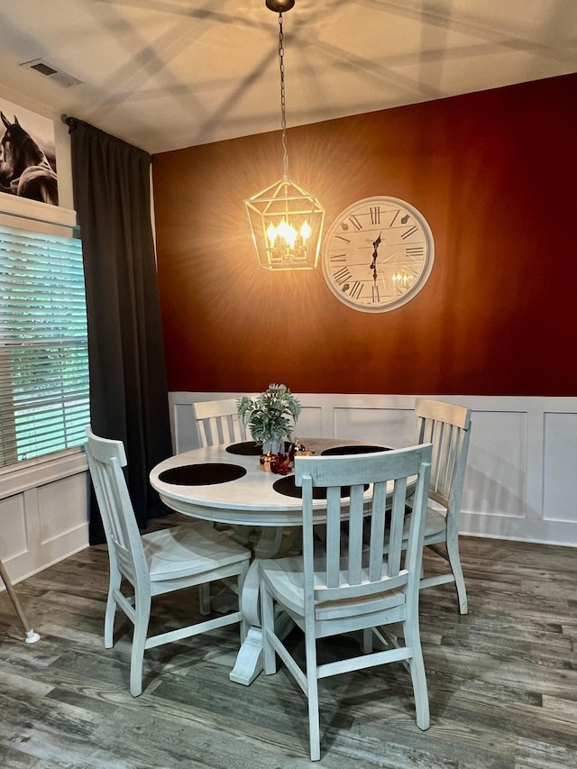 dining space with a decorative wall, wood finished floors, visible vents, and a chandelier