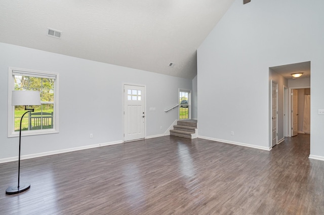 unfurnished living room featuring high vaulted ceiling, dark wood-style flooring, visible vents, and stairway